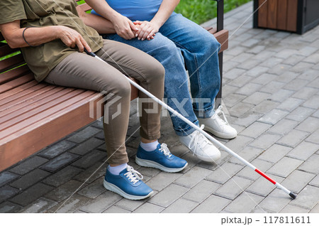 An elderly blind woman and her pregnant daughter are sitting on a bench in the park. Close up legs.  117811611