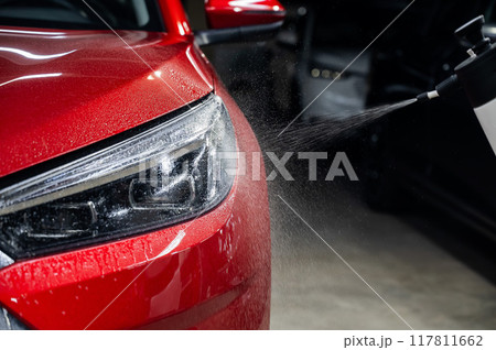A man washes the headlights of a red car with a spray.  117811662