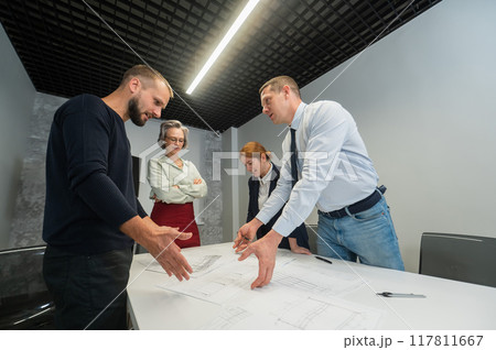 Four business people review and discuss blueprints. Designers engineers at a meeting.  117811667