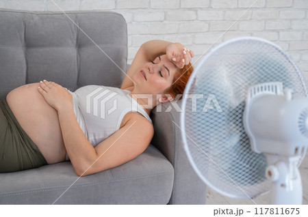 Pregnant woman suffers from heat and lies on the sofa near the electric fan. Pregnant woman suffers from heat and lies on the sofa near the electric fan. 117811675