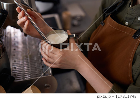 Closeup cropped shot of barista preparing latte with milk foam on coffee machine Closeup cropped shot of barista preparing latte with milk foam on coffee machine 117811748
