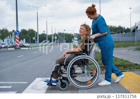 Red-haired nurse pushing an elderly woman in a wheelchair across the road.  117811756