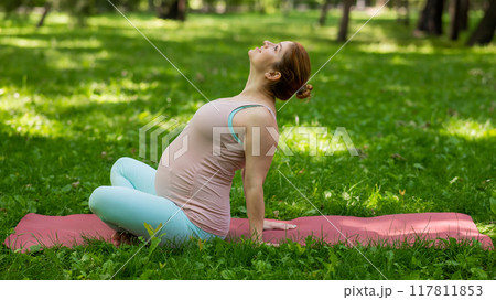 Pregnant caucasian woman doing yoga in the park.  117811853