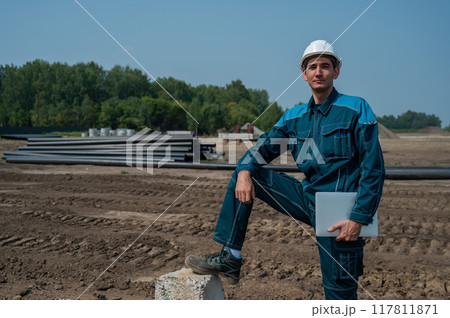 Caucasian male builder in hardhat holding laptop at construction site.  117811871