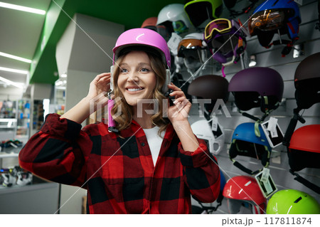 Beautiful young woman trying on new pink protective bike helmet Beautiful young woman trying on new pink protective bike helmet 117811874
