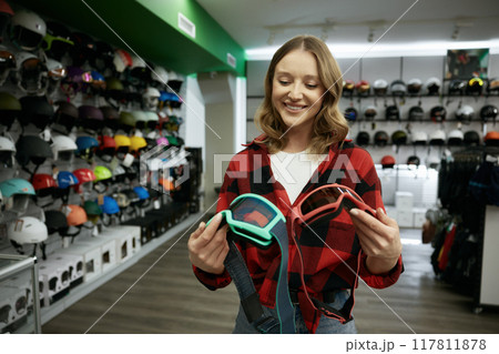 Young smiling woman choosing protective eye goggles mask at sports shop Young smiling woman choosing protective eye goggles mask at sports shop 117811878
