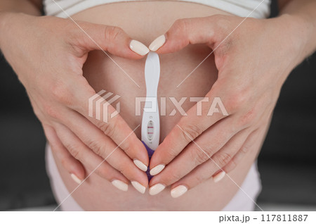 Caucasian woman holding a positive express pregnancy test against the background of her tummy. Caucasian woman holding a positive express pregnancy test against the background of her tummy. 117811887