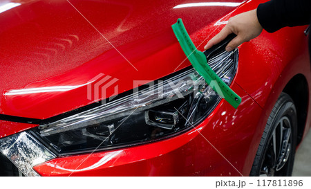A man washes the headlights of a red car with a scraper. A man washes the headlights of a red car with a scraper. 117811896