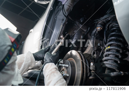 An auto mechanic applies anti-corrosion mastic to the underbody of a car. An auto mechanic applies anti-corrosion mastic to the underbody of a car. 117811906