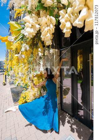 Beautiful Asian ballerina dances against the background of a building decorated with flowers. Vertical photo. Beautiful Asian ballerina dances against the background of a building decorated with flowers. Vertical photo. 117812073