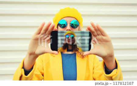 Close up modern stylish happy young woman taking selfie with phone in yellow autumn french beret hat 117812107