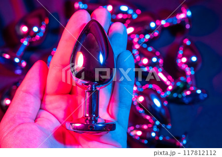 Man holding metal anal plug in neon pink purple light. Man holding metal anal plug in neon pink purple light. 117812112