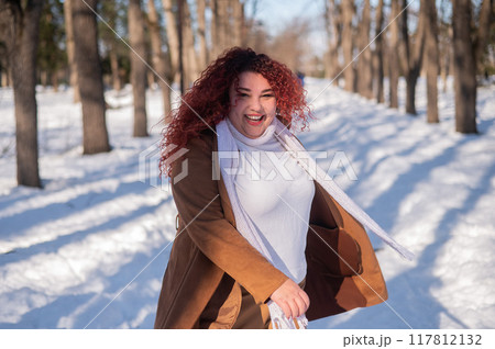 Portrait of an excited red-haired curly fat woman in the park in winter. 117812132