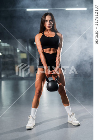 Caucasian woman squats with a kettlebell in the gym. Vertical photo. 117812137