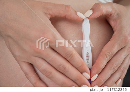Caucasian woman holding a positive express pregnancy test against the background of her tummy. Caucasian woman holding a positive express pregnancy test against the background of her tummy. 117812256