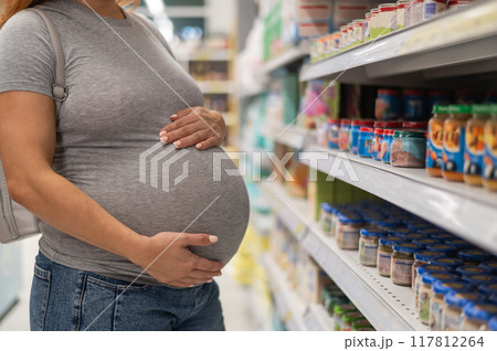 Faceless pregnant woman chooses baby food in the store. Jars with vegetable puree. Faceless pregnant woman chooses baby food in the store. Jars with vegetable puree. 117812264