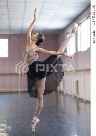 Graceful Asian ballerina in a beige bodysuit and black skirt is rehearsing in a dance class.  117812310