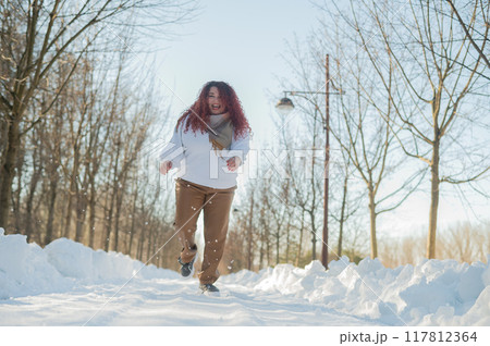 Smiling chubby redhead woman running in park in winter. Smiling chubby redhead woman running in park in winter. 117812364