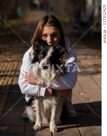 Caucasian woman hugging border collie in autumn park. Portrait of a girl with a dog. 117812420