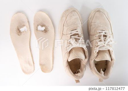 Heavily used white sneaker with detached sole and removed insole. Visible dirt, wear, and holes. Sole and insole separated, lying beside the sneaker, 117812477