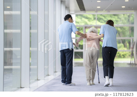 杖をついて歩くシニア女性を支える介護スタッフ　後ろ姿 117812623