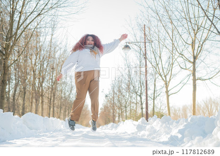 Smiling plump redhead woman jumping in park in winter.  117812689