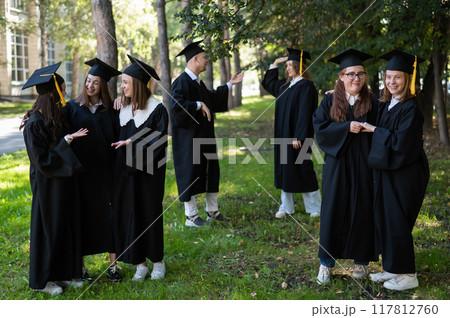 A group of graduates in robes congratulate each other on their graduation outdoors. 117812760