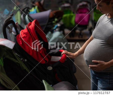 Red-haired pregnant woman chooses a stroller in a children's store.  117812787