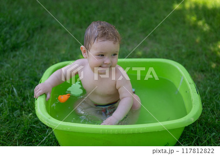 Cute baby boy bathes in a basin outdoors in summer. Cute baby boy bathes in a basin outdoors in summer. 117812822