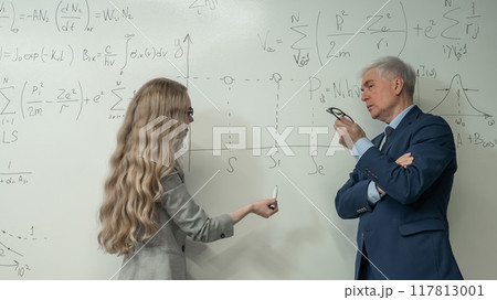 Female student answers a question from an elderly professor at a white board. Female student answers a question from an elderly professor at a white board. 117813001