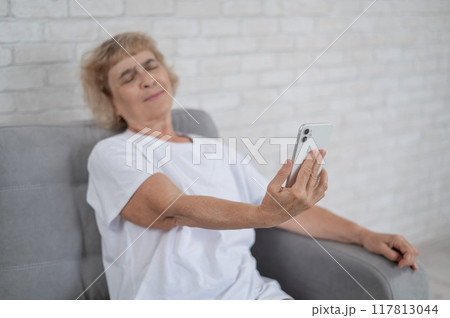 An elderly Caucasian woman suffers from farsightedness and tries to read a message on a smartphone with her arm outstretched. An elderly Caucasian woman suffers from farsightedness and tries to read a message on a smartphone with her arm outstretched. 117813044
