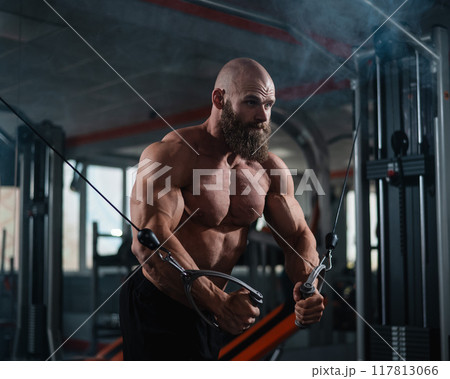 Bald Caucasian bodybuilder training chest using cable crossover in gym. Bald Caucasian bodybuilder training chest using cable crossover in gym. 117813066