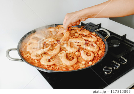 man adding some shrimps to a spanish fideua man adding some shrimps to a spanish fideua 117813895