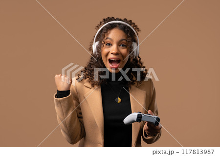 Zoomer teenager girl playing online video game, winning with gamepad on beige Zoomer teenager girl playing online video game, winning with gamepad on beige 117813987