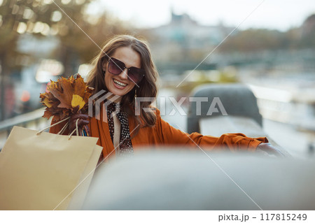 happy elegant woman in brown trench coat with shopping bags 117815249