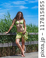 Summer elegance: Young woman in a green bikini on a wooden walkway 117815855