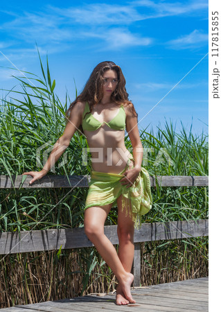 Summer elegance: Young woman in a green bikini on a wooden walkway Summer elegance: Young woman in a green bikini on a wooden walkway 117815855