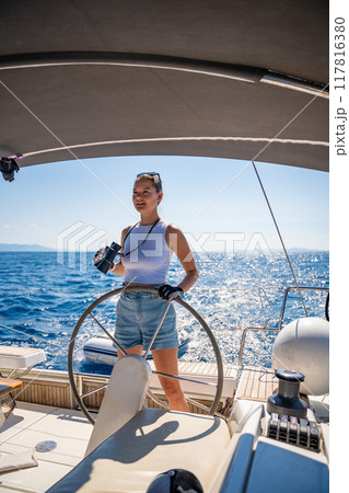 Young female captain on the yacht looking through binoculars during sailing boat control. Travel and active life. Yachting 117816380