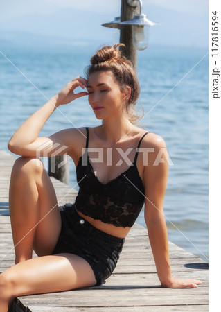 Sun-kissed: Woman in a black lace top enjoys the summer breeze by the lake Sun-kissed: Woman in a black lace top enjoys the summer breeze by the lake 117816594