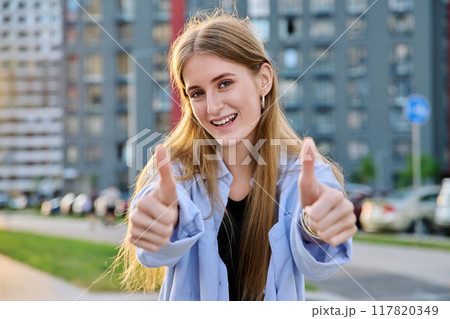 Young happy cheerful woman showing thumbs up, outdoors. 117820349