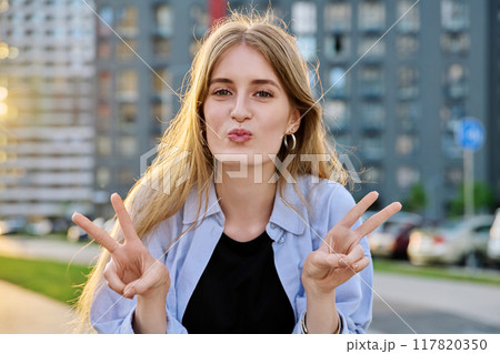 Young beautiful happy cheerful woman showing victory gesture with hands, outdoors. 117820350