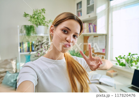 Close-up selfie portrait of teenage cheerful female looking at web camera 117820476