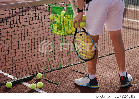 Tennis player holding racket and ball standing near net on court, close up Tennis player holding racket and ball standing near net on court, close up 117824395