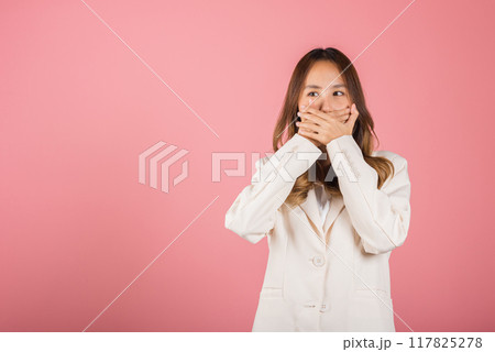 Asian happy portrait beautiful young woman standing smiling surprised excited her covering mouth with hands see only eyes and looking to camera on pink background with copy space for text 117825278