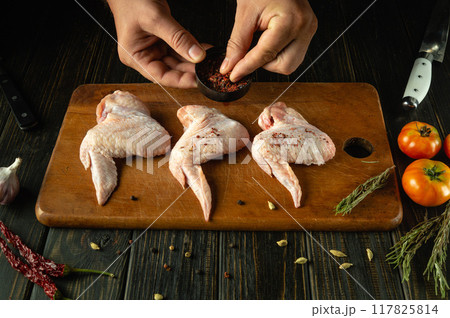 Butcher hands prepares chicken wings for frying with spices. Preparation of cooking Buffalo wings on the kitchen table 117825814