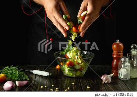 Chef preparing vegetable mix for breakfast. Preparing salad with fresh vegetables on kitchen table. The cook hands mixing chopped vegetables in bowl 117825819