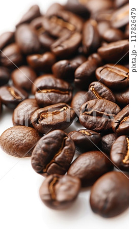 The glossy, dark-brown coffee beans lay scattered across a clean white surface 117826479