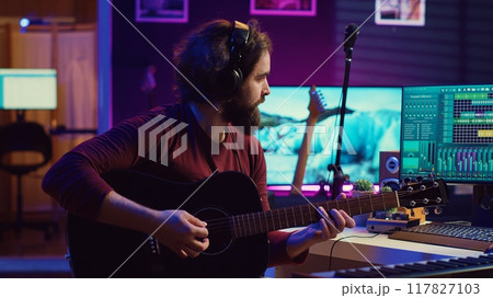 Skilled artist recording his guitar song to mix on daw software, working with electronic soundboard equipment. Audio engineer producing soundtracks or sound effects in his home studio. Camera A. 117827103