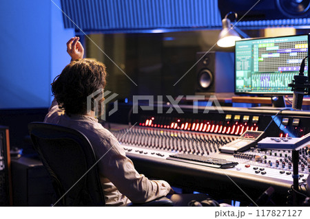 Sound designer counting down for singer in vocal booth to start performance for recording session, producing new music in control room. Skilled audio engineer operating panel board. 117827127