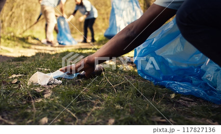 Citizens reducing pollution and illegal disposal by tidying the environment and recycling plastic with the right instruments. Volunteers clearing garbage from the forest. Close up. Camera B. Citizens reducing pollution and illegal disposal by tidying the environment and recycling plastic with the right instruments. Volunteers clearing garbage from the forest. Close up. Camera B. 117827136